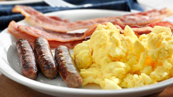 Scrambled eggs, sausage and bacon on a white plate