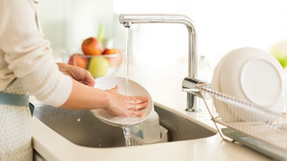 Woman washing dishes in the sink with a bowl of fruit on the counter