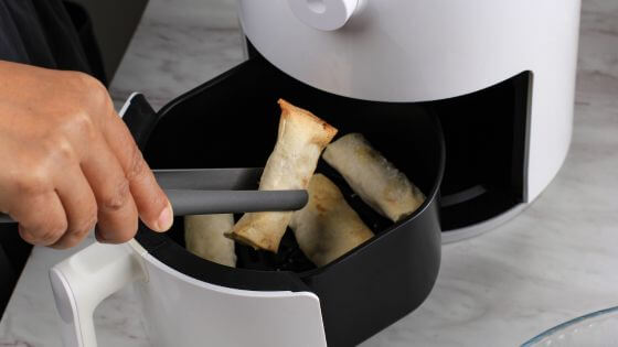 Putting egg rolls in the air fryer with tongs