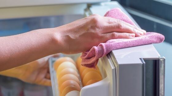woman wiping refrigerator with pink cloth