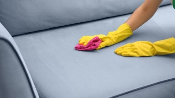 woman with yellow cleaning gloves wiping a grey couch