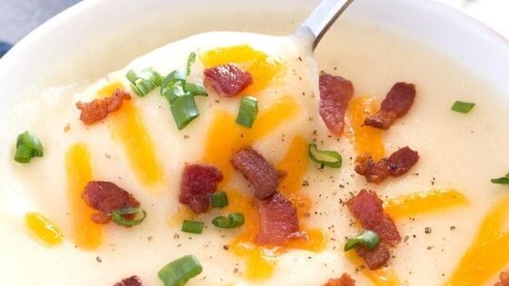 Potato soup with bacon bits and cheese in white bowl