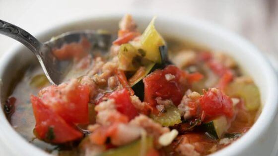 Sausage and zucchini soup in white bowl with spoon