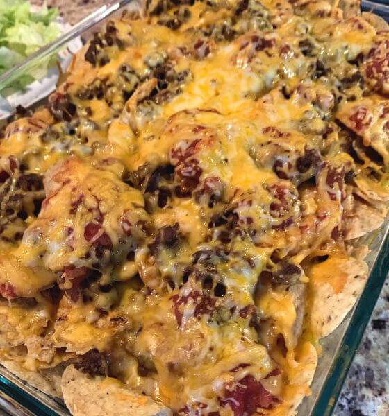 prepared layered nacho casserole in glass baking dish with lettuce on the side