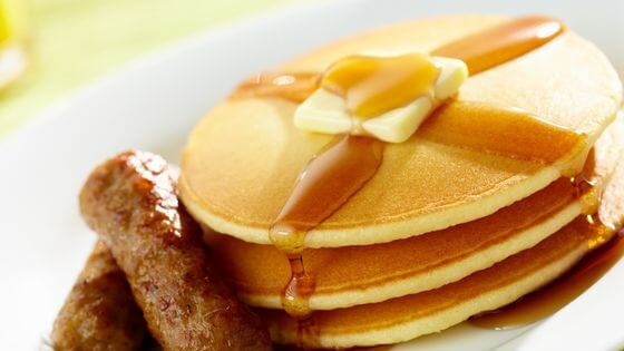 Pancakes with butter and syrup on white plate with sausage links