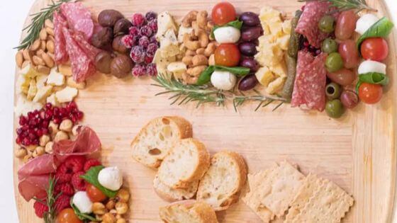 Charcuterie board shaped like a candy cane with crackers, vegetables, cheese and meat