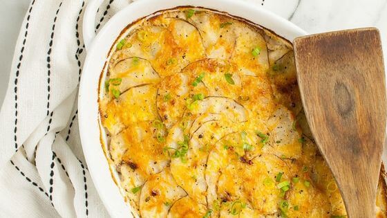 Scalloped potatoes in white dish with wood spoon on side