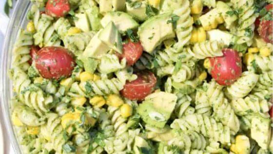 Avocado salad with pasta and tomatoes in glass bowl