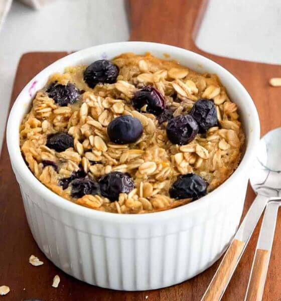 Blueberry oatmeal in white bowl with utensils on the side