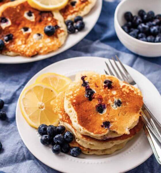 Blueberry pancakes on white plate with lemons and blueberries on the side.