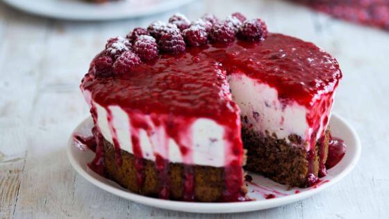 Raspberry cheesecake on white plate with raspberries on top