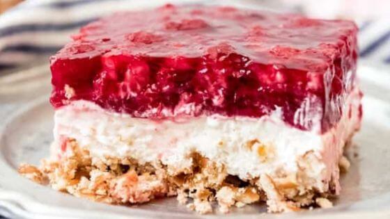 Raspberry bar with cream cheese and pretzel crust on white plate