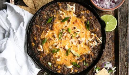 Black bean dip in black skillet with cheese on top and red onions on the side in a dish