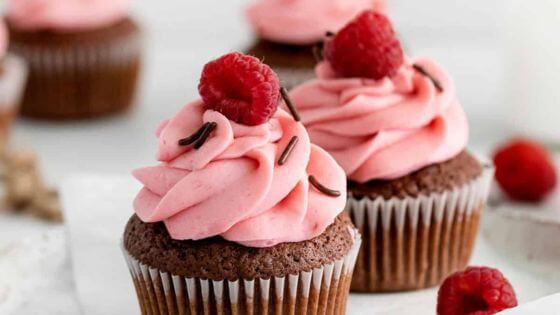 Chocolate cupcakes with raspberry frosting with chocolate sprinkles and a raspberry on top.