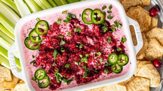 Cranberry jalapeno dip in white dish with sliced jalapenos and cracker and celery on the side