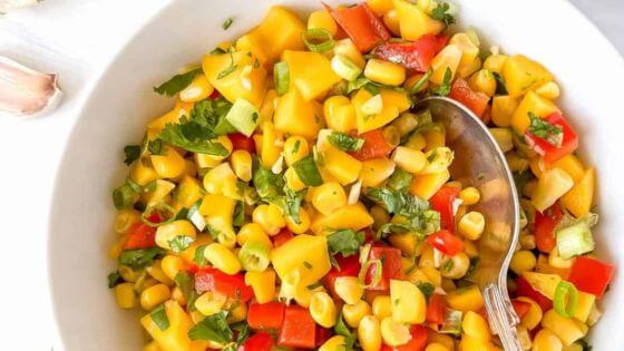 Corn and mango salsa in white bowl with spoon