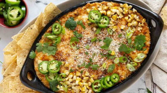 Mexican street corn dip in black baking dish with tortilla chips on the side