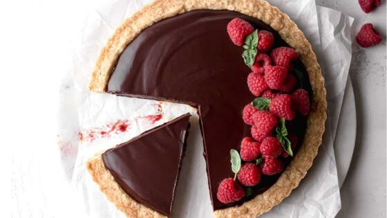 Raspberry chocolate tart with a slice cut out of it and raspberries on top.