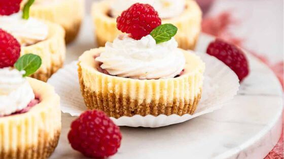 Raspberry mini cheesecake on cupcake wrapper with raspberries on the side.