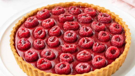 A raspberry tart with raspberries on the top sitting on a white plate