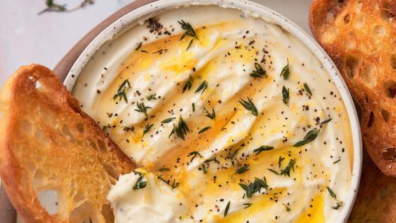 Whipped ricotta dip in white bowl with crusty bread on the side for dipping