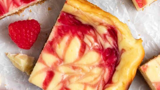 Raspberry cheesecake bars on wax paper with a raspberry on the side.