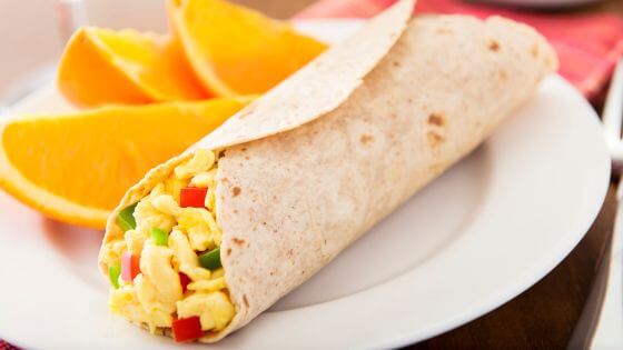 Breakfast burrito on a white plate with orange slices