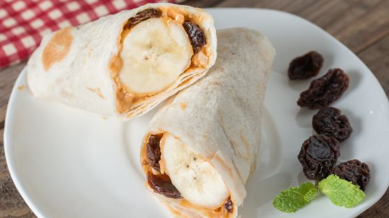 Tortilla shell with peanut butter, bananas and raisins on a white plate