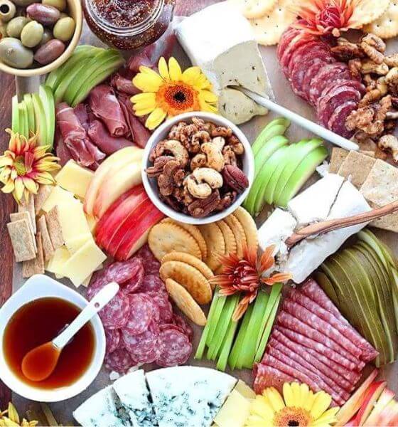 Fall charcuterie board with sunflowers, crackers, nuts, salami, cheese, apples and olives.