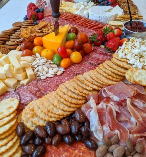 Grazing table with crackers, salami, ham, cheese, tomatoes, strawberries and popcorn.