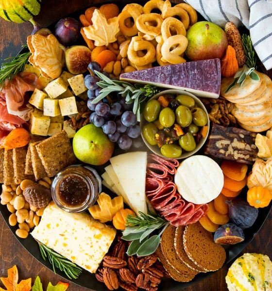 Thanksgiving charcuterie board on round platter with olives, crackers, cheese, salami, and grapes.