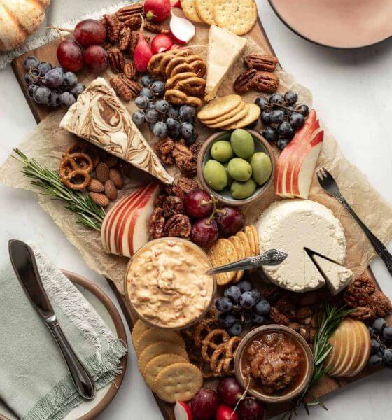 Vegan cheese board with cheese, grapes, blueberries, crackers, apples, pretzels and spread.
