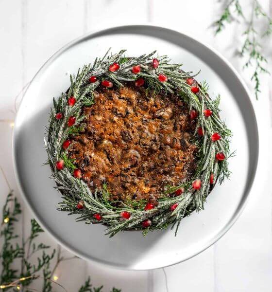 Christmas fruit cake on white plate with wreath and red berries around it