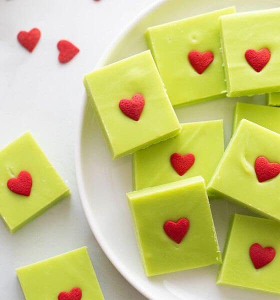 Green Grinch inspired fudge with red hearts on a white plate