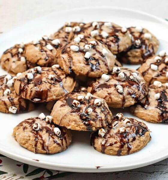 Hot chocolate cookies with mini marshmallows and chocolate sauce drizzle on a white plate