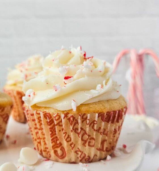 White Chocolate cupcakes with crushed peppermint on top with candy canes in the background.