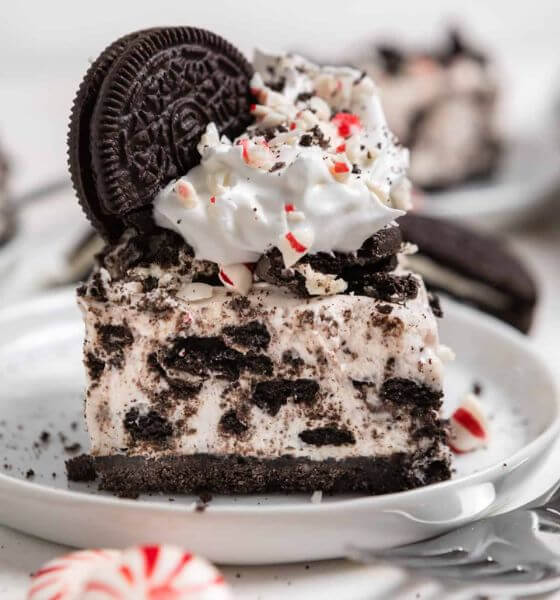 Peppermint Oreo cheesecake with Oreos, whipped cream and crushed peppermint on a white plate