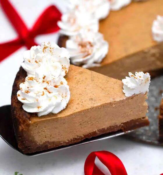 Gingerbread cheesecake on cake serving utensil with whipped cream on top