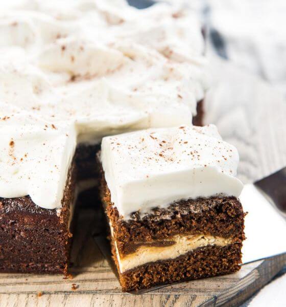 Cheesecake stuffed gingerbread cake with white frosting on wood platter