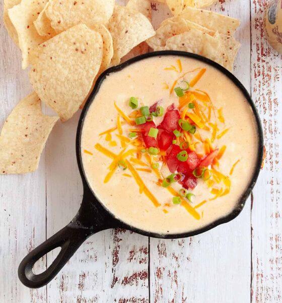 Beer cheese dip in skillet with cheese and tomatoes on top and tortilla chips on the side