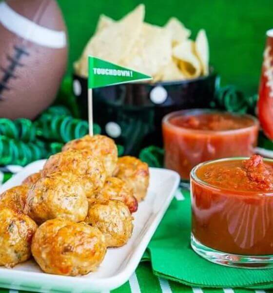 Chicken parmesan meatballs on white platter with marinara sauce in glass dish on the side.
