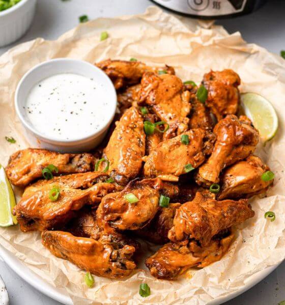 Chicken wings on paper with white bowl with dipping sauce.
