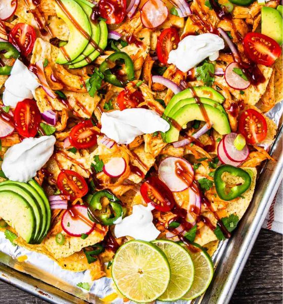 Barbecue chicken nachos on sheet pan with avocado, jalapeno, sour cream, and tomatoes.