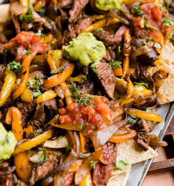 Steak fajita nachos on sheet pan with guacamole, tomatoes and peppers.