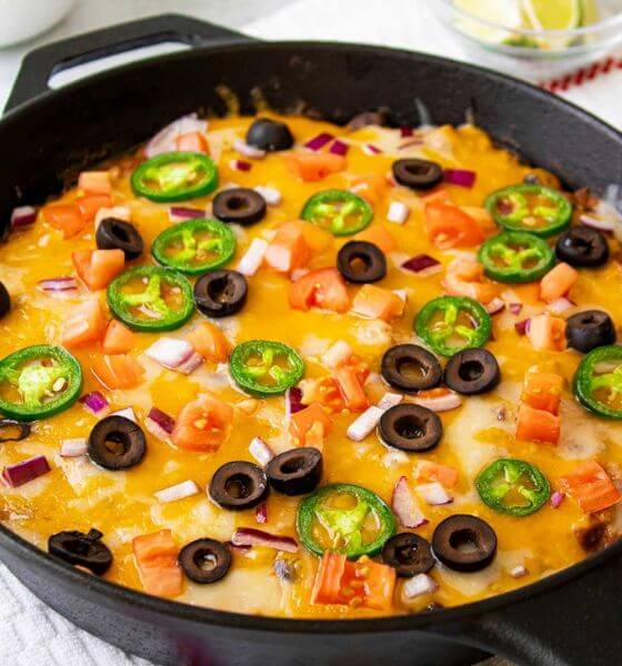 Taco dip in skillet with black olives and jalapenos on top