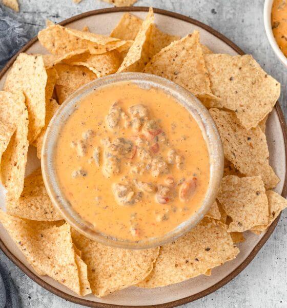 Sausage and melted cheese dip on white and brown plate with tortilla chips on the side.