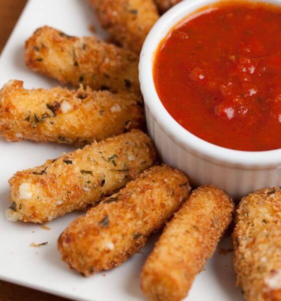 Mozzarella sticks on white plate with a marinara sauce in white bowl