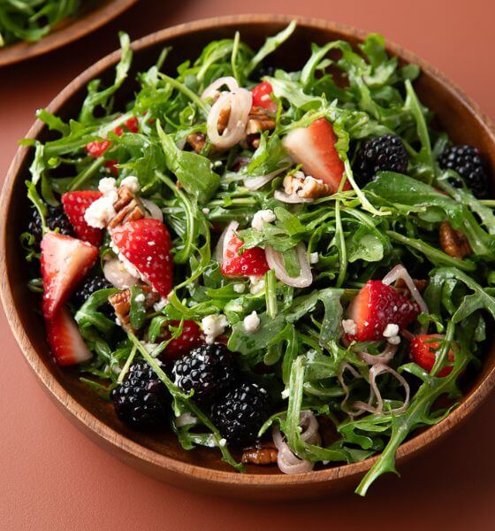 Arugula salad in wood bowl with blackberries and strawberries