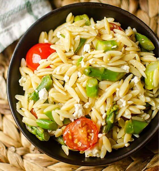 Lemon orzo salad with peas and tomatoes in a black bowl
