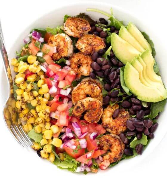 Shrimp avocado salad for spring in white bowl with corn, black beans, onions and tomatoes.